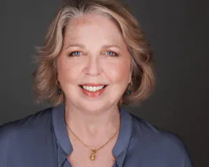 Smiling middle-aged woman with light hair against a dark background.