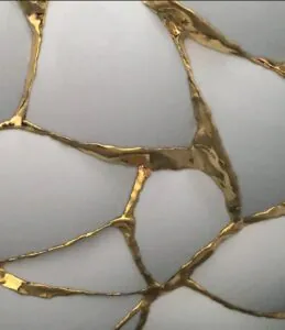 Close-up of white ceramic pieces joined by gold lacquer in a kintsugi style.