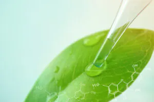 Close-up of a dropper applying liquid onto a green leaf with chemical formulas.