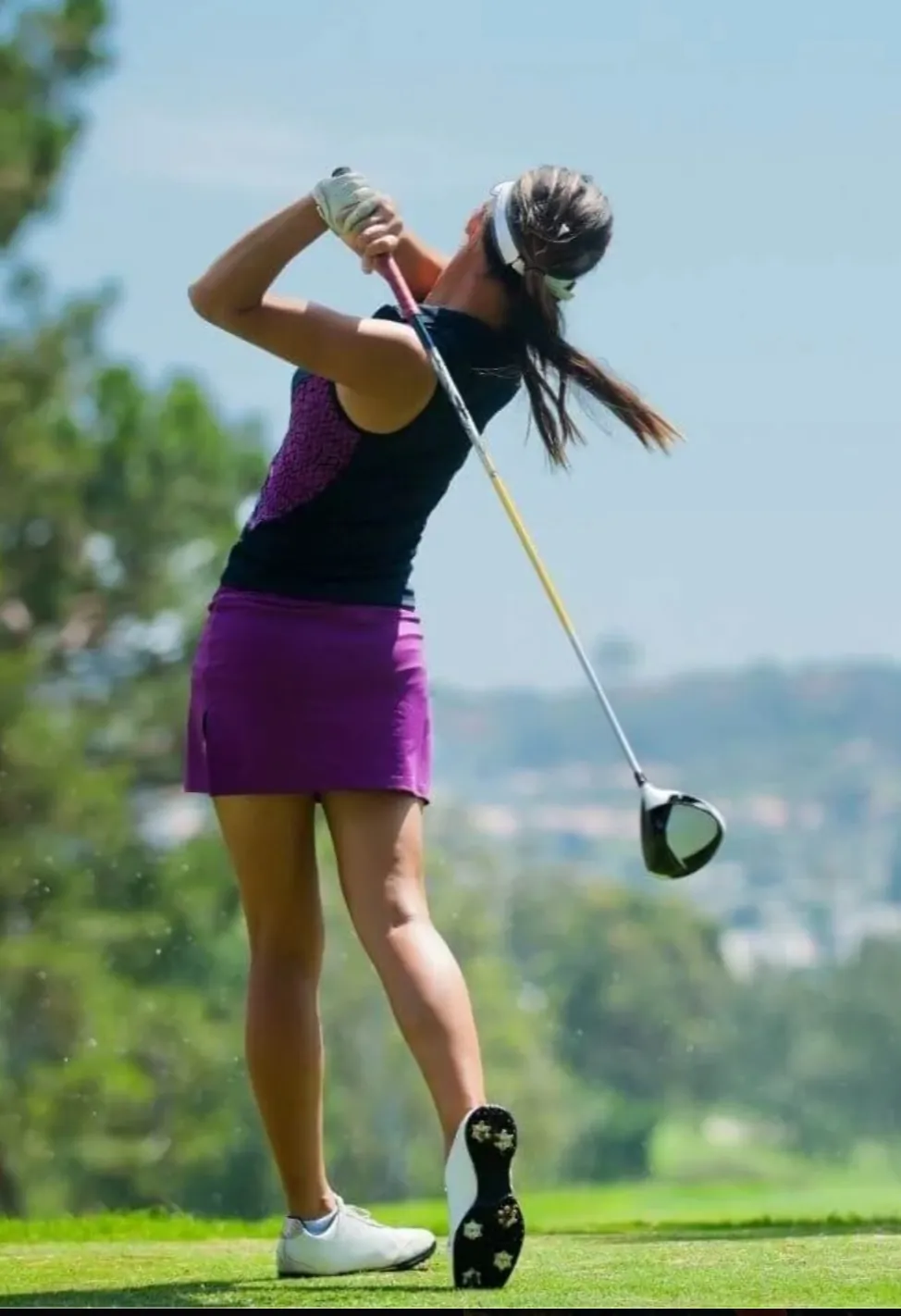 Woman in purple dress swinging a golf club on a sunny day. Woman in purple dress swinging a golf club on a sunny day.
